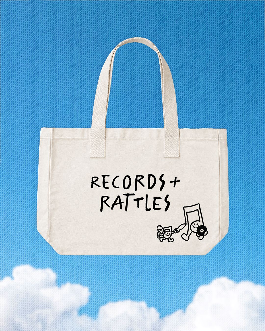 Beige tote bag with 'Records + Rattles' text and music note graphic on a blue sky background