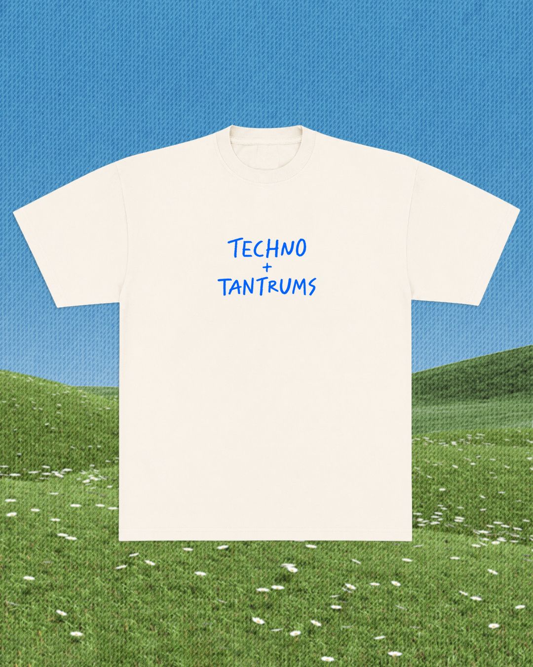 White t-shirt with 'TECHNO + TANTRUMS' text on a grassy field with blue sky background